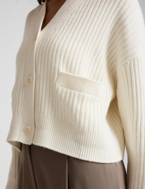 woman wearing a cream cardigan on a plain background. 