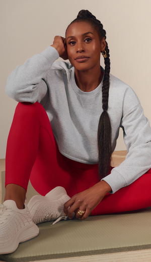 Issa Rae sitting down wearing red spacedye leggings and a grey sweatshirt. 